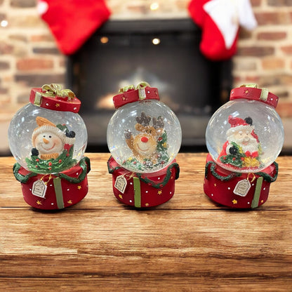 Weihnachtliche Schneekugeln mit Schneemann, Rentier und Nikolaus, dekorativ vor einem Kamin arrangiert.