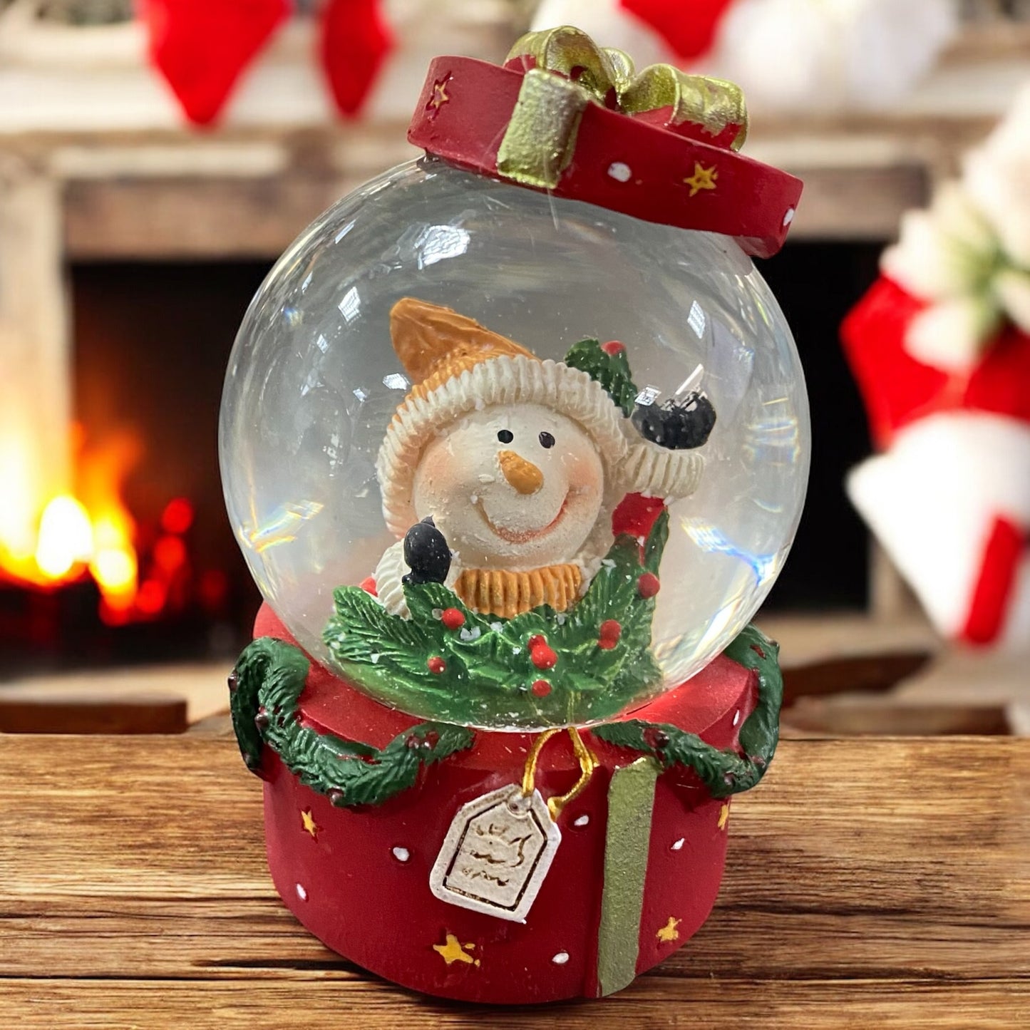 Schneekugel mit fröhlichem Schneemann, auf rotem Geschenksockel vor festlicher Kaminumgebung präsentiert.