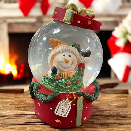 Schneekugel mit fröhlichem Schneemann, auf rotem Geschenksockel vor festlicher Kaminumgebung präsentiert.