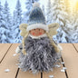 Flauschige Stoff-Engelfigur mit blauer Strickmütze und weißen Flügeln auf einem Holztisch, im Hintergrund verschneite Bäume.