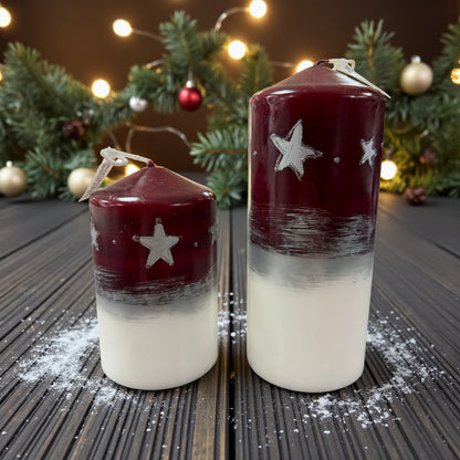 Weihnachtliches Kerzenset aus zwei Größen in Rot-Weiß mit silbernen Sternen, stimmungsvoll dekoriert mit Kunstschnee, Tannengirlande und Lichterkette.