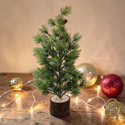 Ein kleiner künstlicher Tannenbaum mit Zapfen steht auf einem Holzsockel in weihnachtlicher Dekoration.