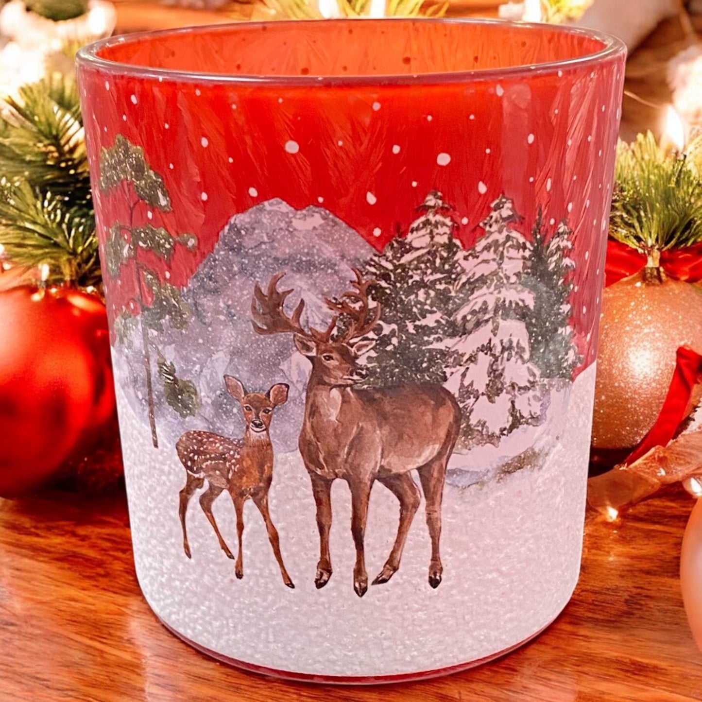 Kleiner roter Teelichthalter mit winterlicher Szene und Hirschen, festlich dekoriert mit Weihnachtskugeln
