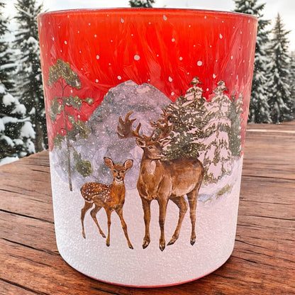 Großer roter Teelichthalter mit Hirschfamilie im verschneiten Wald, weihnachtlich arrangiert mit Lichtern und Deko

