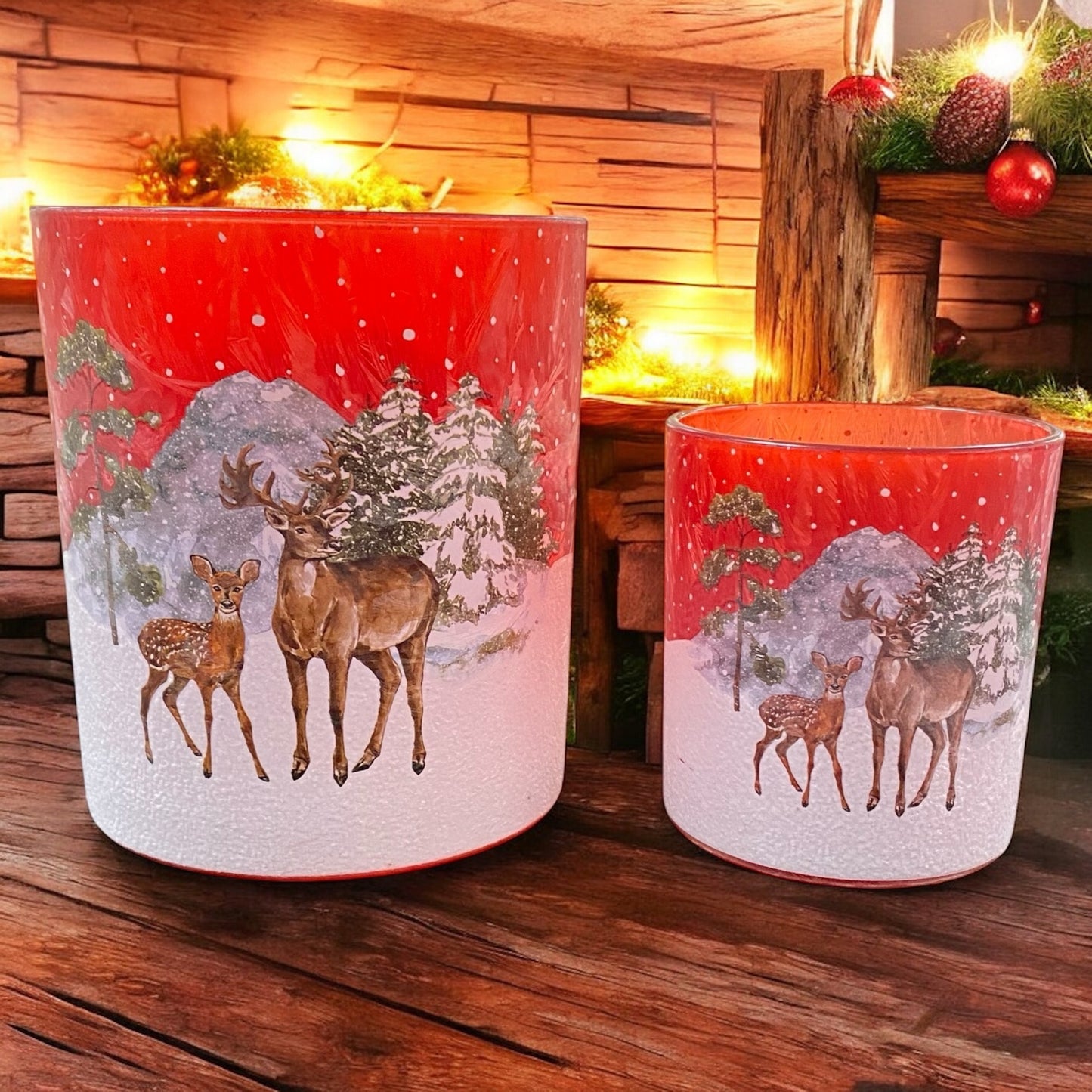 Zwei rote Teelichthalter mit Hirschmotiv in verschneiter Waldlandschaft, stimmungsvoll beleuchtet auf Holz präsentiert.