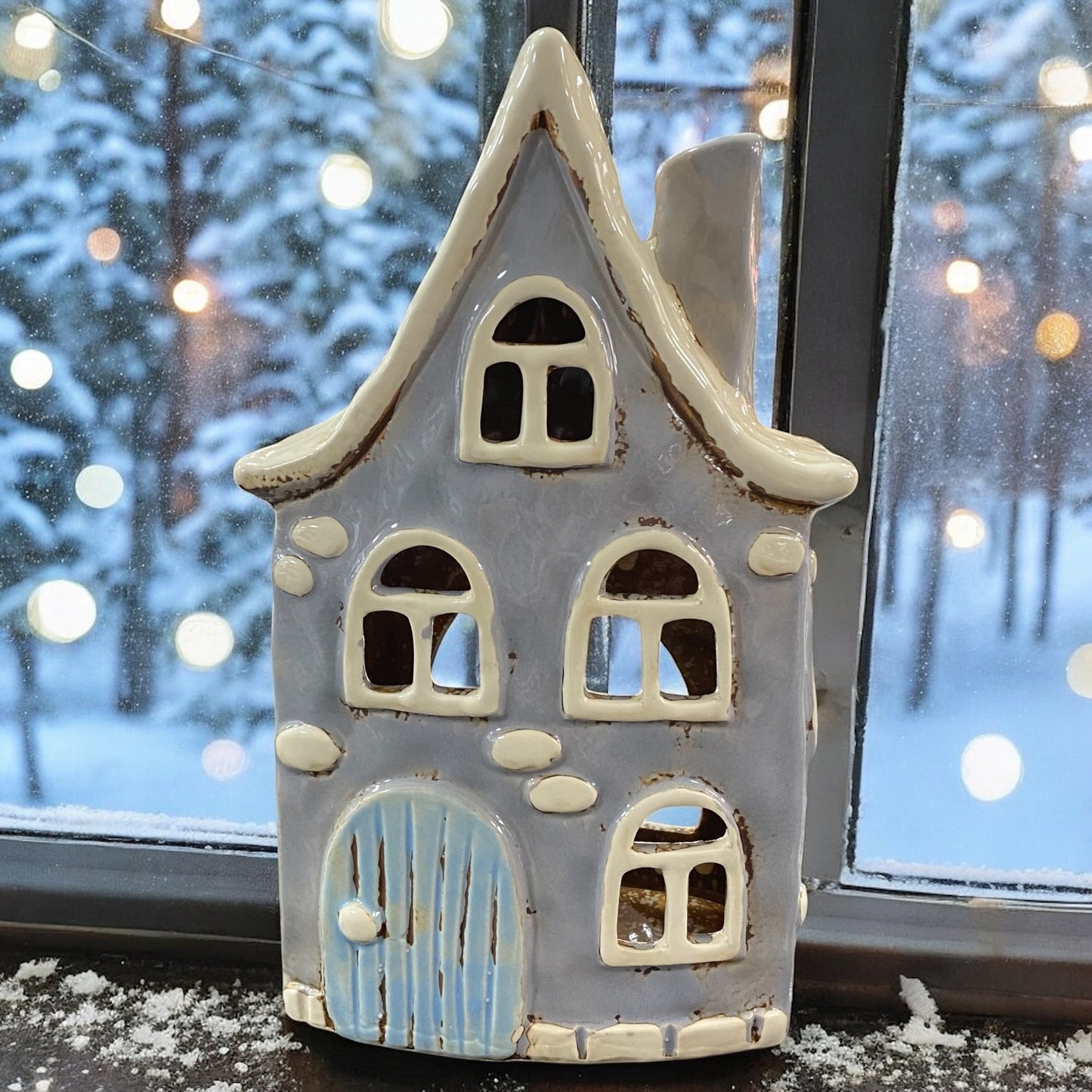 Formano Windlicht in Hausform aus blauer Keramik, winterlich auf Fensterbank mit Schneelandschaft arrangiert.
