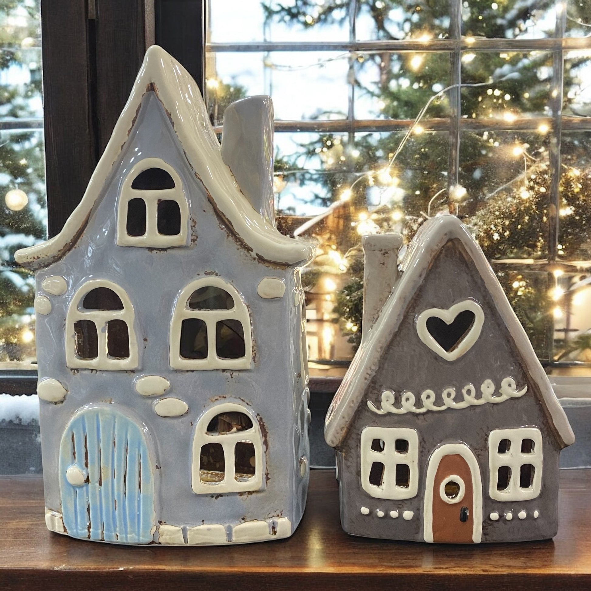 Zwei Formano Windlichter in Hausform aus Keramik, stimmungsvoll vor einem Fenster mit Lichterdekoration arrangiert.