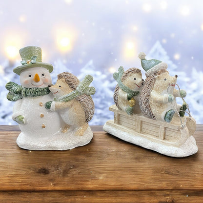 Niedliche Winterfiguren: Igel auf Schlitten und Igel mit Schneemann, stimmungsvoll vor verschneitem Hintergrund arrangiert.