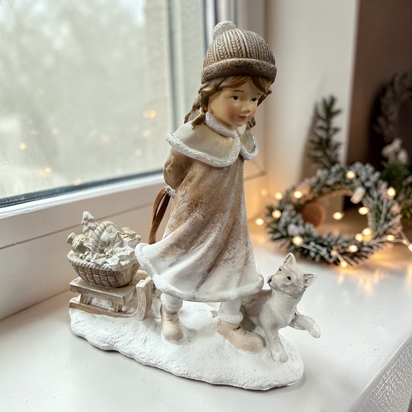Eine dekorative Figur zeigt ein Kind, das einen Schlitten zieht, neben einer Katze auf einer winterlichen Basis.