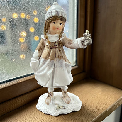 Eine dekorative Figur zeigt ein stehendes Kind in winterlicher Kleidung, das einen Stern in der Hand hält.