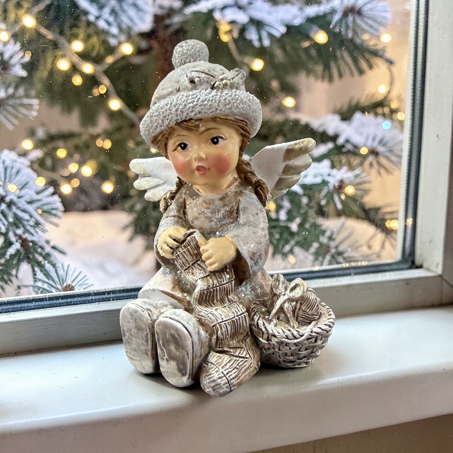 Eine dekorative Figur zeigt ein sitzendes Kind mit Flügeln neben einem Korb auf einer winterlichen Basis.