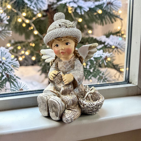 Eine dekorative Figur zeigt ein sitzendes Kind mit Flügeln neben einem Korb auf einer winterlichen Basis.