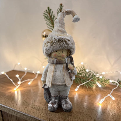 Eine dekorative Mädchenfigur mit Fellmütze hält einen Stern in den Händen und steht auf einer dekorierten Holzfläche.