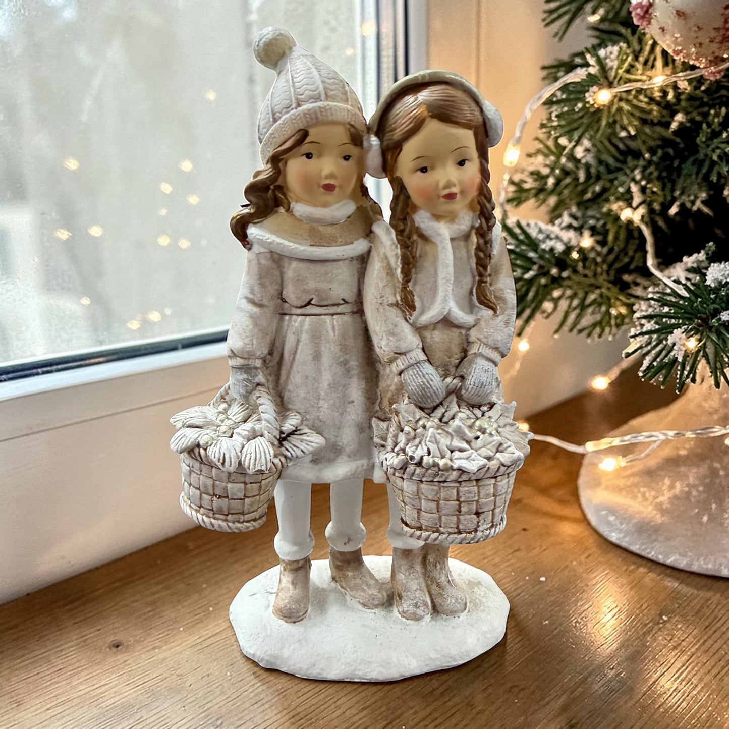 Eine dekorative Figur zeigt zwei stehende Kinder mit Körben in winterlicher Kleidung.