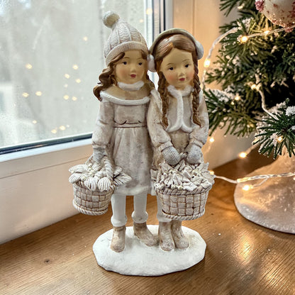 Eine dekorative Figur zeigt zwei stehende Kinder mit Körben in winterlicher Kleidung.