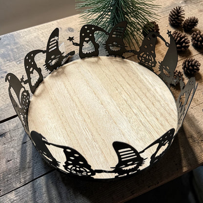 Ein schwarzes Tablett mit dekorativem Wichtelrand liegt auf einem Holztisch und wird von Tannenzweigen und Zapfen in einer natürlichen Weihnachtsdekoration eingerahmt.
