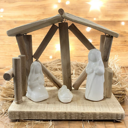 Rustikale Holzkrippe mit weißen Figuren von Maria, Josef und Jesuskind, stimmungsvoll vor warmem Lichterhintergrund arrangiert.