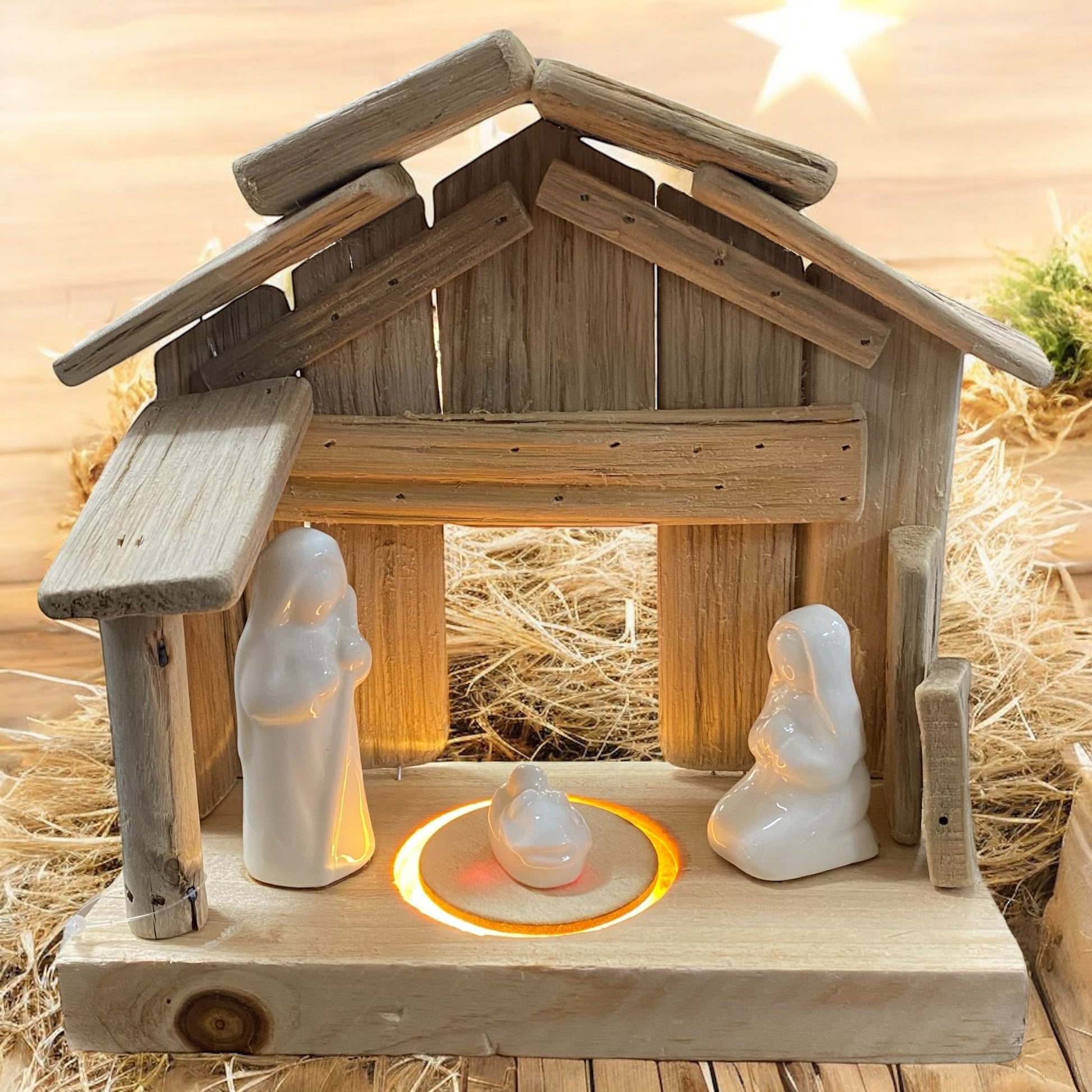 Beleuchtete Holzkrippe mit weißen Figuren von Maria, Josef und Jesuskind, stimmungsvoll vor warmem Lichterhintergrund arrangiert.