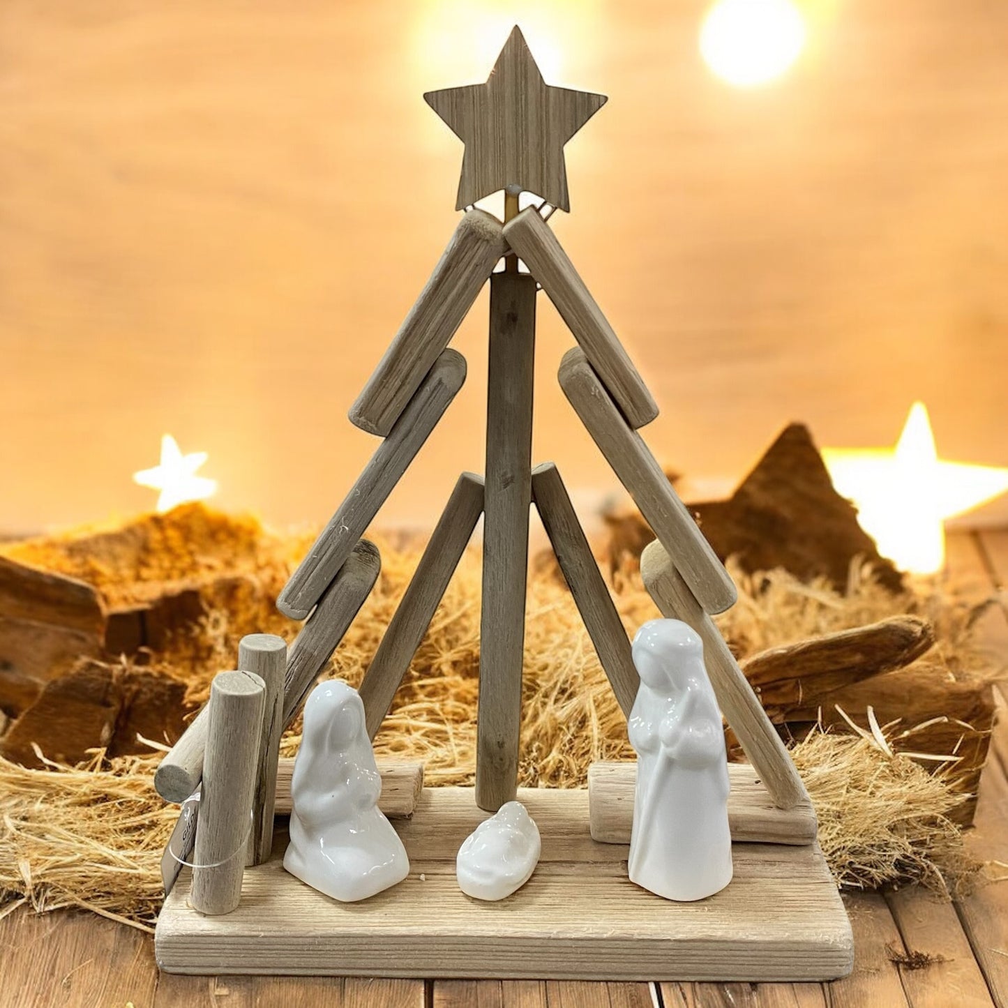 Holzkrippe in Form eines Tannenbaums mit weißen Figuren, stimmungsvoll vor warmem Lichterhintergrund arrangiert.