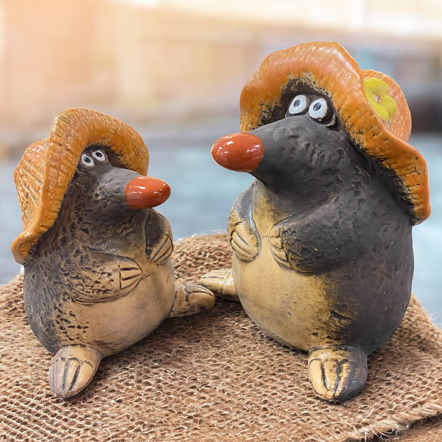 Zwei Gilde Maulwurf-Figuren aus Keramik mit Hüten, dekorativ auf Jutesack im rustikalen Ambiente arrangiert.