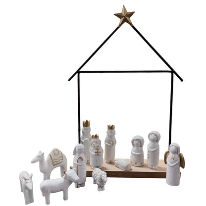 Moderne Krippenszene mit Keramikfiguren in Weiß und Gold, arrangiert auf Holzsockel innerhalb eines schwarzen Metallrahmens in Hausform, freigestellt vor weißem Hintergrund.