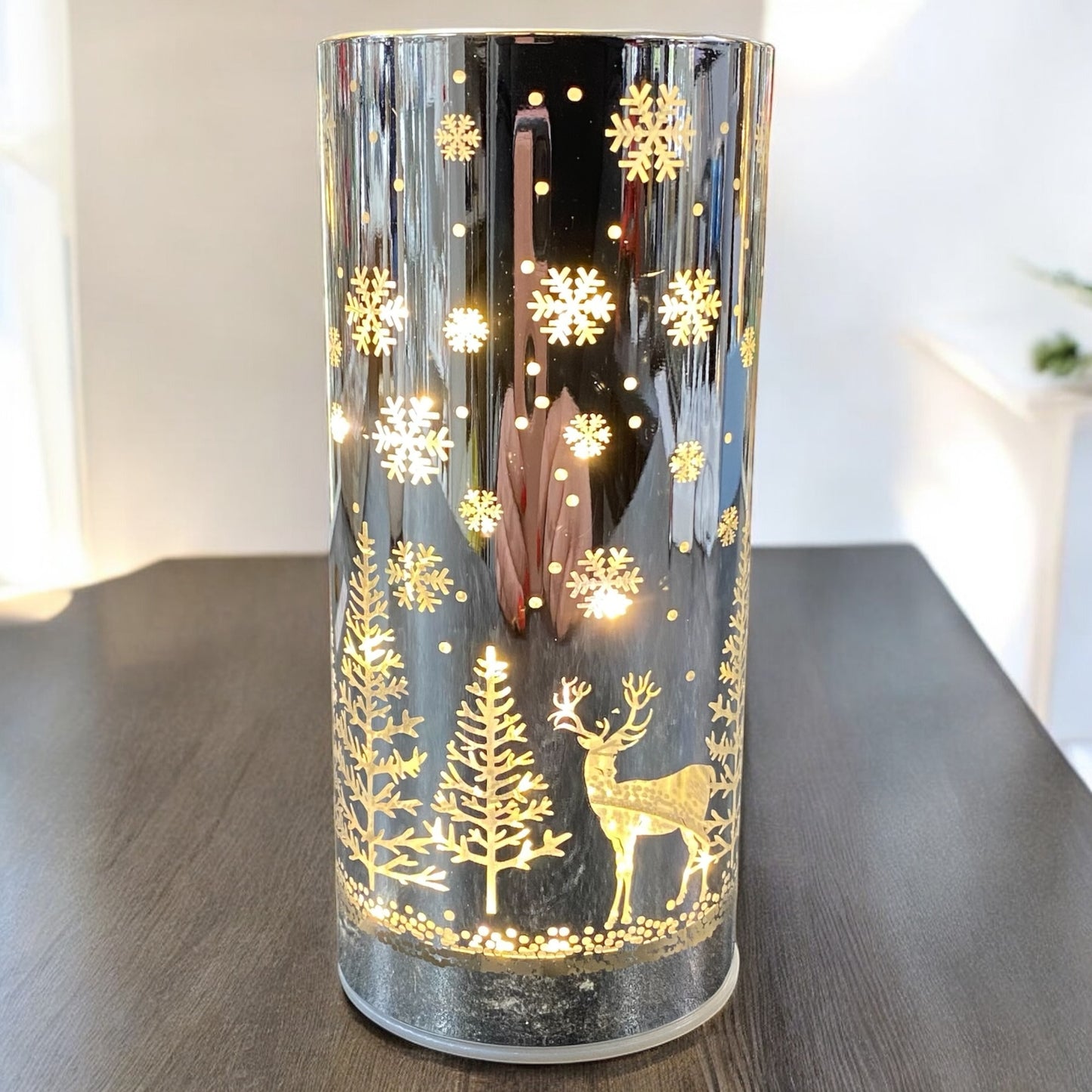 Leuchtendes silbernes LED-Deko-Licht mit goldenem Hirsch- und Schneeflockenmuster auf einem dunklen Tisch in winterlicher Umgebung.