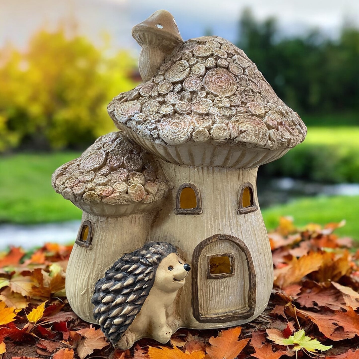 Kleines Pilzhaus mit LED-Beleuchtung und Igel, herbstliche Dekoration auf Blätterteppich im Garten.
