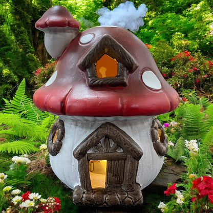 Rotes Pilzhaus mit LED-Beleuchtung, märchenhafte Herbstdekoration im Garten zwischen Farnen und Blüten.