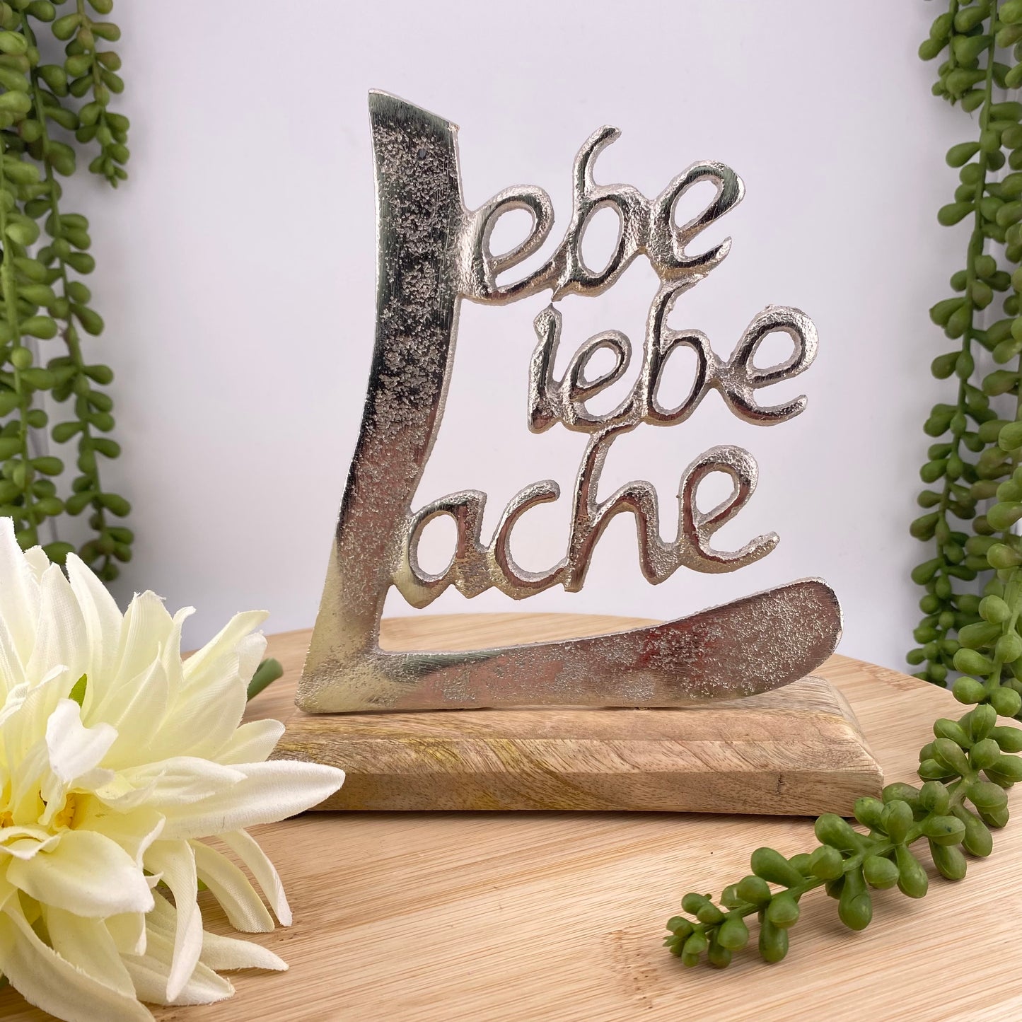 Deko Aufsteller auf Holzsockel mit Schrift Lebe Liebe Lache aus Aluminium im Ambiente platziert, 17cm groß.