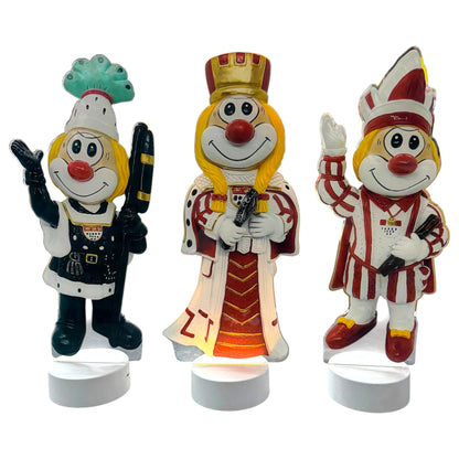 Drei Schmitzens Karneval Deko Lampen als Dreigestirn mit Bauer, Jungfrau und Prinz auf weißen Sockeln vor weißem Hintergrund.