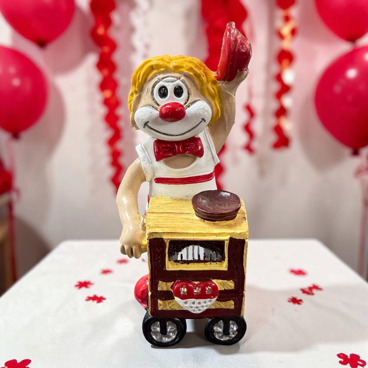 Karneval Deko Clown Die Schmitzens Leierkasten mit rotem Leierkasten vor rot-weißer Karnevalsdekoration.