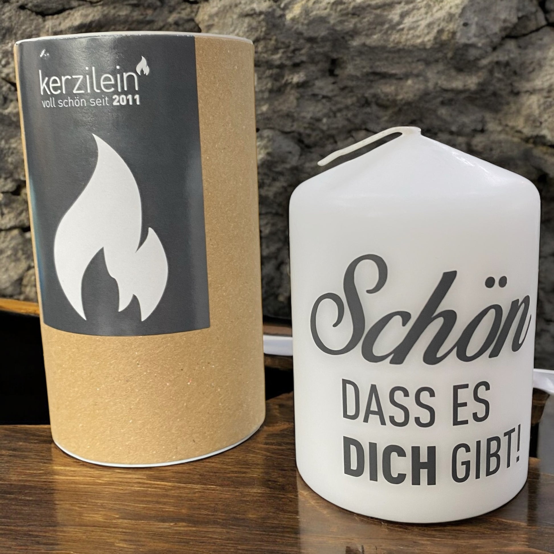 Weiße Stumpenkerze mit schwarzem Schriftzug „Schön, dass es dich gibt!“ im Ambiente