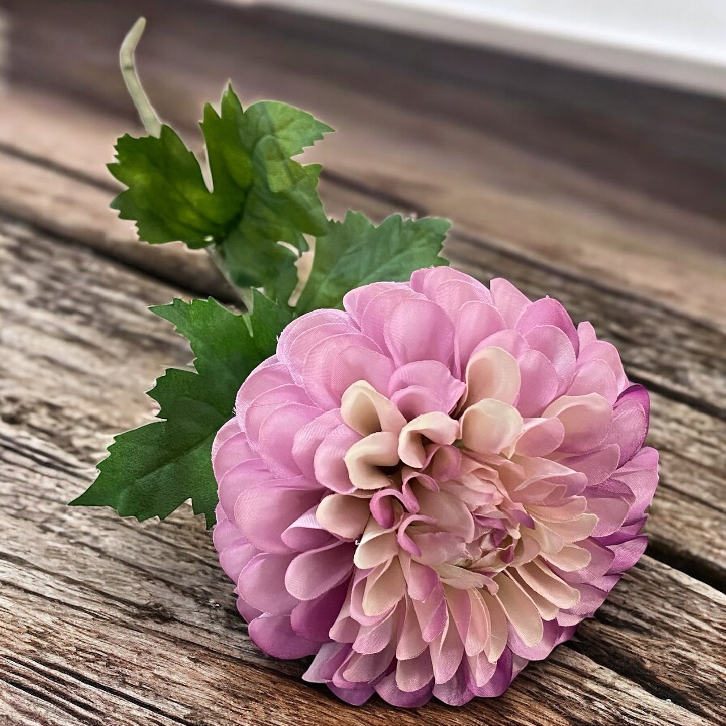 Eine künstliche Dahlienblüten in Lila mit grünem Blattwerk und Stiel im Ambiente