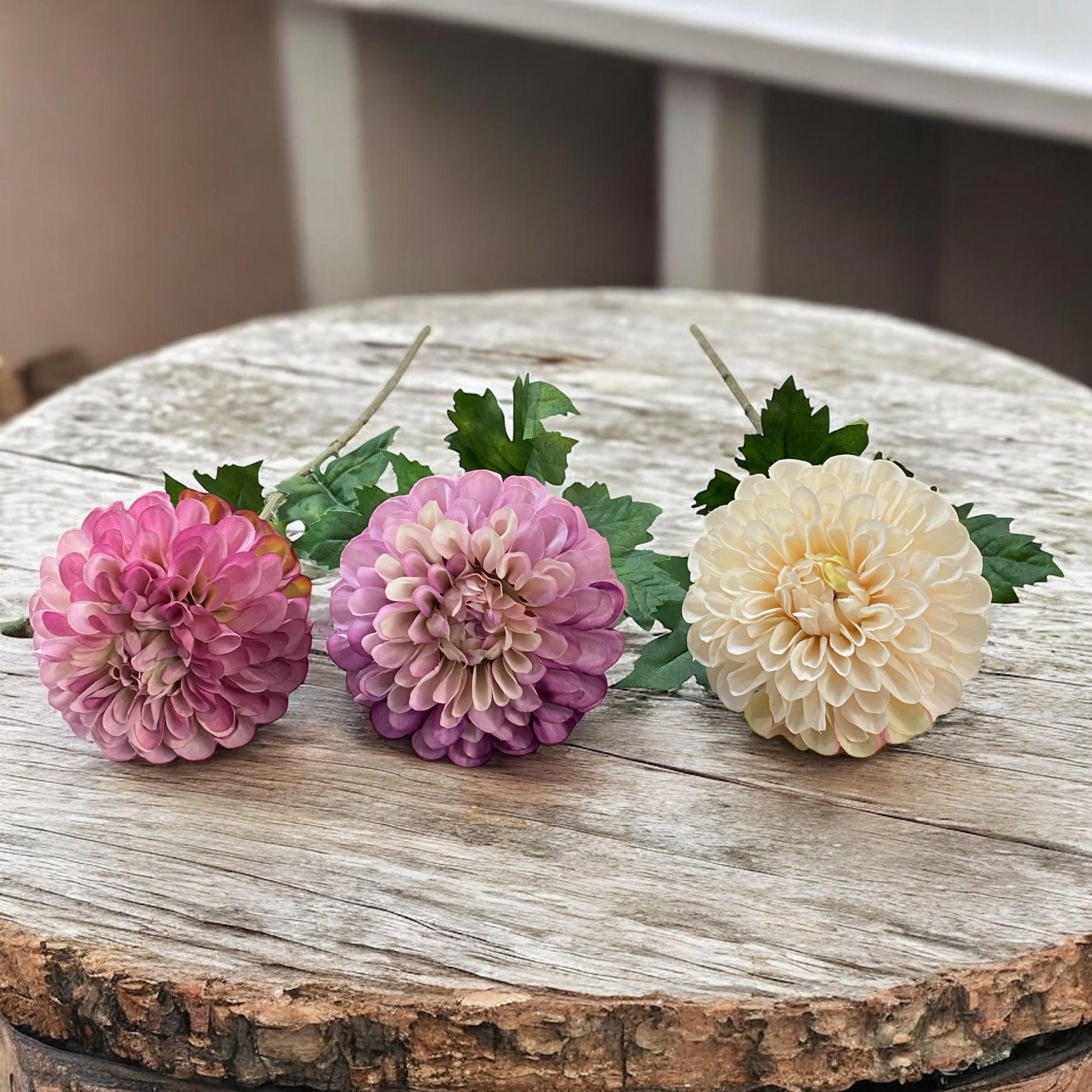 Drei künstliche Dahlienblüten in Rosa, Lila und Creme mit grünem Blattwerk und Stiel im Ambiente