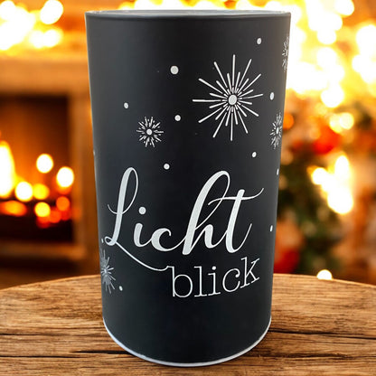 Schwarze LED-Lichtsäule mit dem goldenen Schriftzug „Lichtblick“, strahlend vor Kaminfeuer und weihnachtlicher Stimmung.