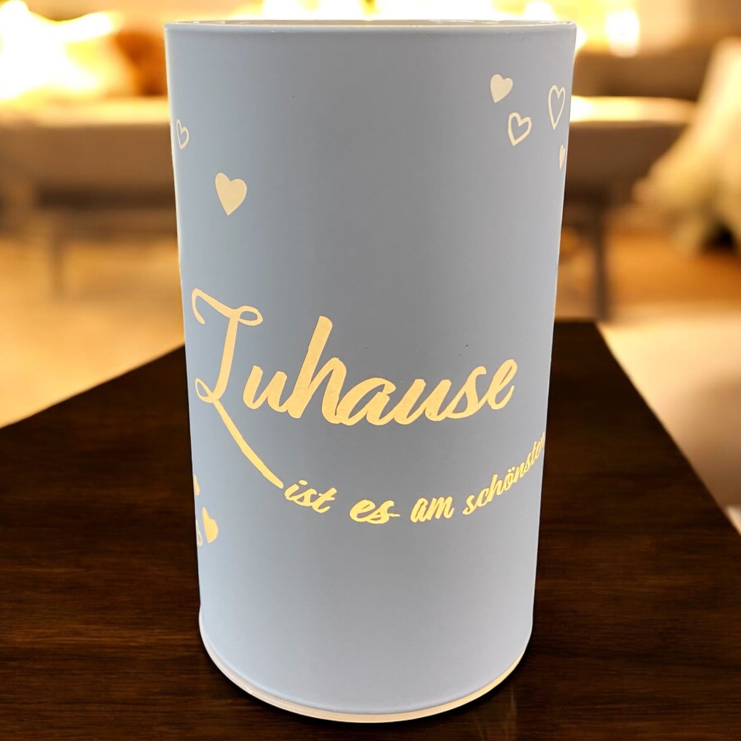 Weiße LED-Lichtsäule mit dem goldenen Spruch „Zuhause ist es am schönsten“ in gemütlicher Wohnraum-Atmosphäre.