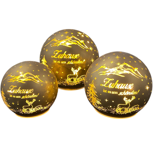 Drei goldene LED-Dekokugeln mit dem Spruch „Zuhause ist es am schönsten“ und Rentiermotiv in verschiedenen Größen.