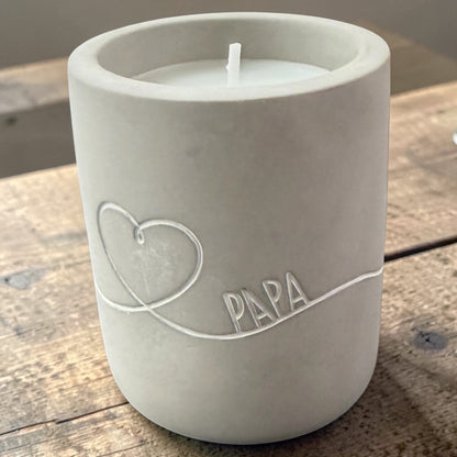Graue Betonkerze mit eingraviertem Schriftzug „PAPA“ und Herzmotiv auf einer Holzoberfläche.