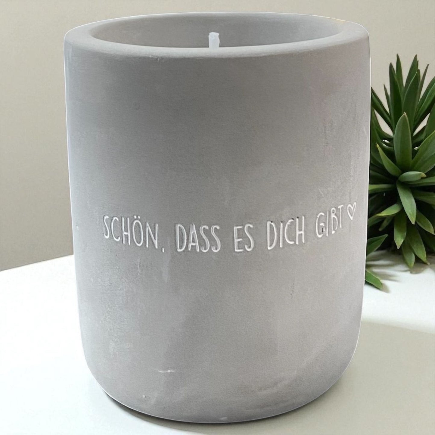 Eine Mea Living Kerze mit Spruch "Schön, dass es dich gibt" in Betonoptik, 8 cm hoch, im Ambiente