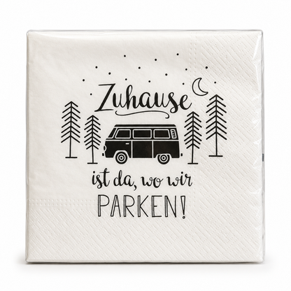 Cremeweiße Papierservietten mit schwarzem Wohnmobil, Bäumen und dem Spruch „Zuhause ist da, wo wir parken!“ vor weißem Hintergrund.