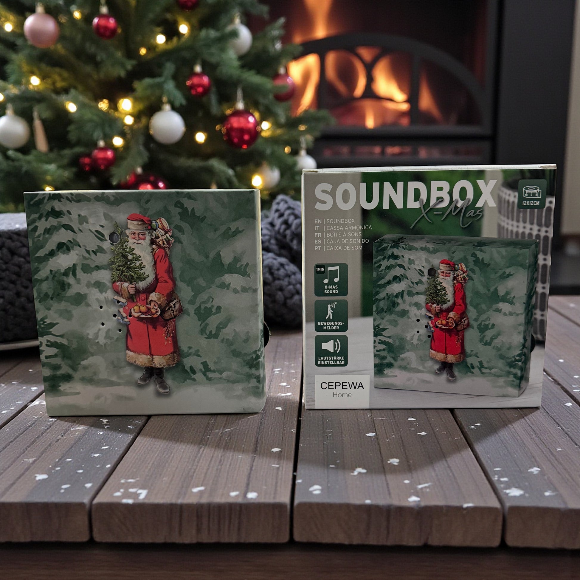 Eine weihnachtliche Soundbox mit Weihnachtsmann-Motiv steht neben ihrer Verpackung auf einem Holztisch vor Kamin und Weihnachtsbaum.