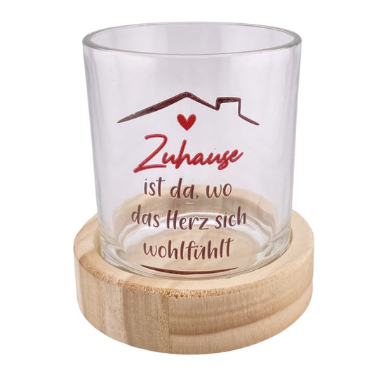 Ein Teelichthalter mit rundem Holzsockel und Glas mit rotem Schriftzug "Zuhause ist da, wo das Herz sich wohlfühlt" ist vor weißem Hintergrund platziert