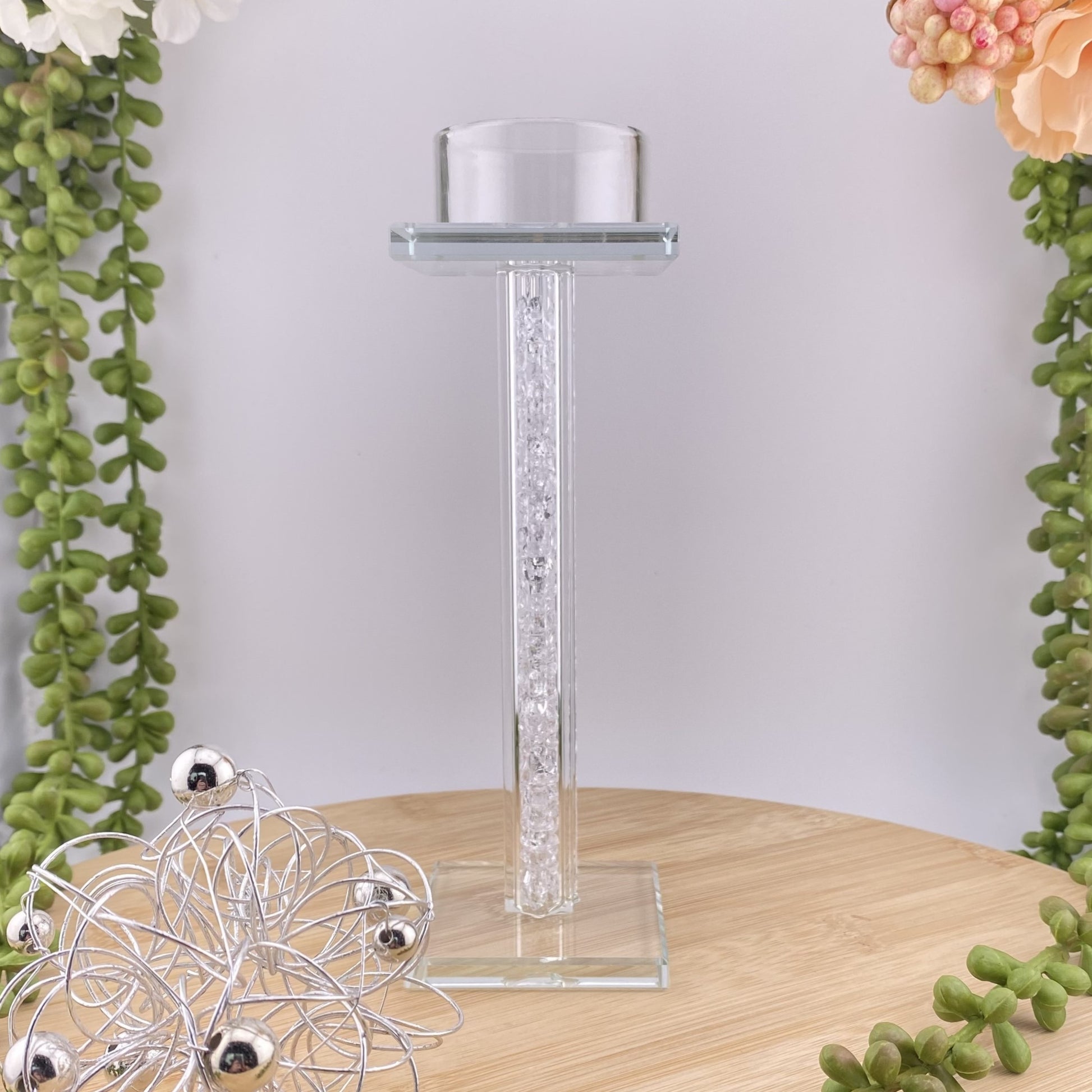 Ein großer Teelichthalter aus Glas mit quadratischem Sockel. Oben kann ein Teelicht platziert werden. Im Ambiente platziert. 