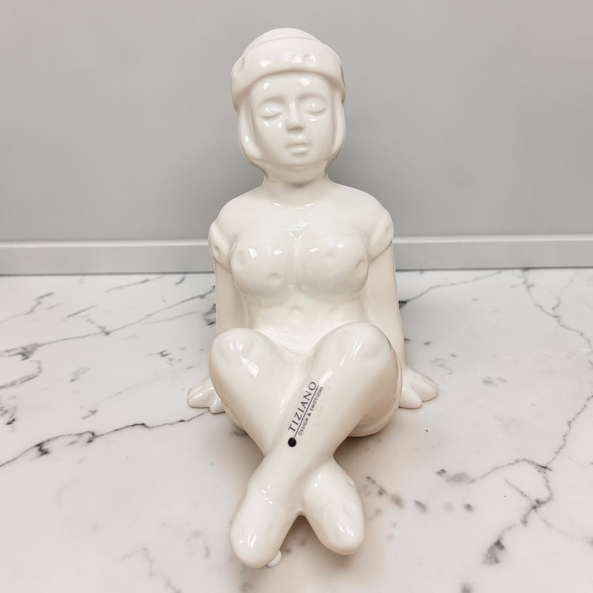 Cremeweiße Tiziano Keramik Dekofigur Badenixe Marie sitzend, 21 cm hoch, auf einer hellen Oberfläche vor grauem Hintergrund.