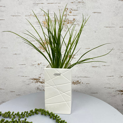 Eine creme-weiße Keramik Deko Blumenvase Übertopf ist im Ambiente mit Blumen platziert. Die Deko Vase hat diverse Linien als Einkerbungen.