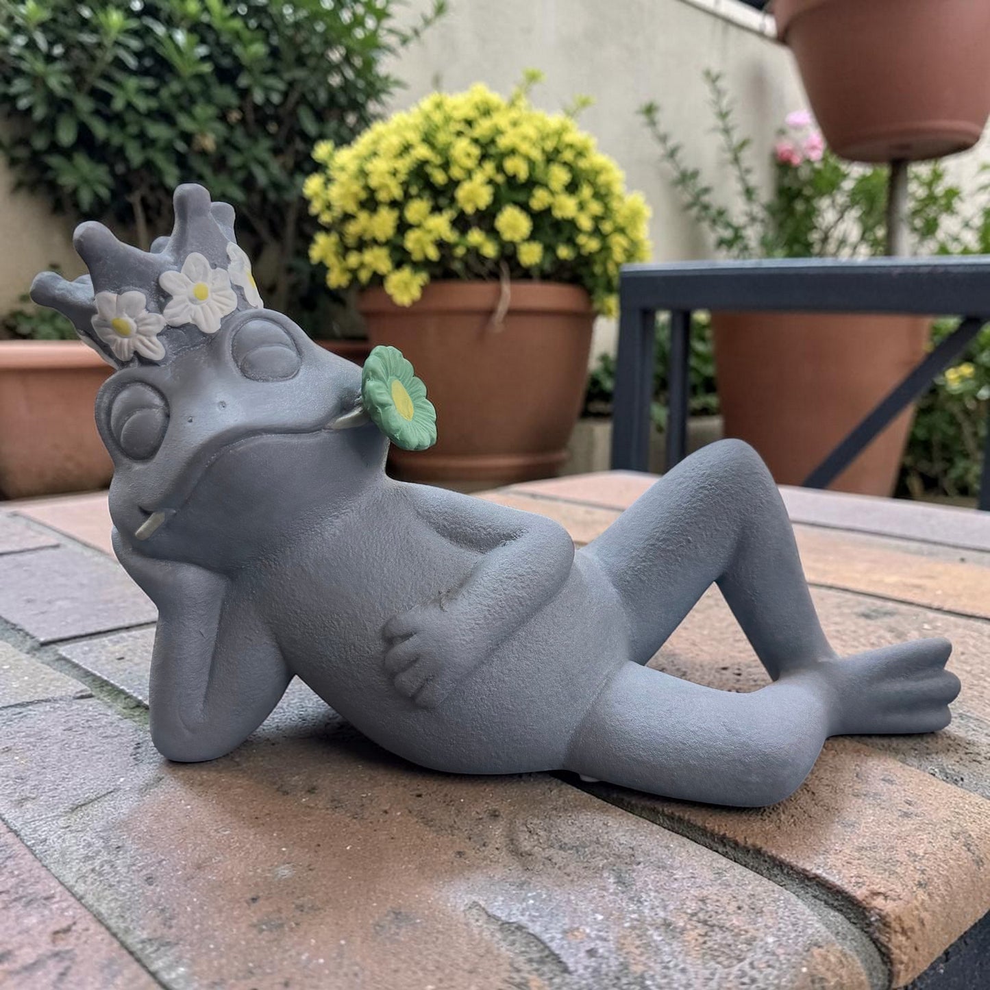 Grauer Frosch in entspannter Liegepose mit geschlossenen Augen und grüner Blume im Mund.