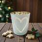 Hellgraues Glasgefäß mit Herzmotiv und goldfarbener Innenseite dekorativ auf einem Holztisch vor weihnachtlichem Hintergrund platziert.

