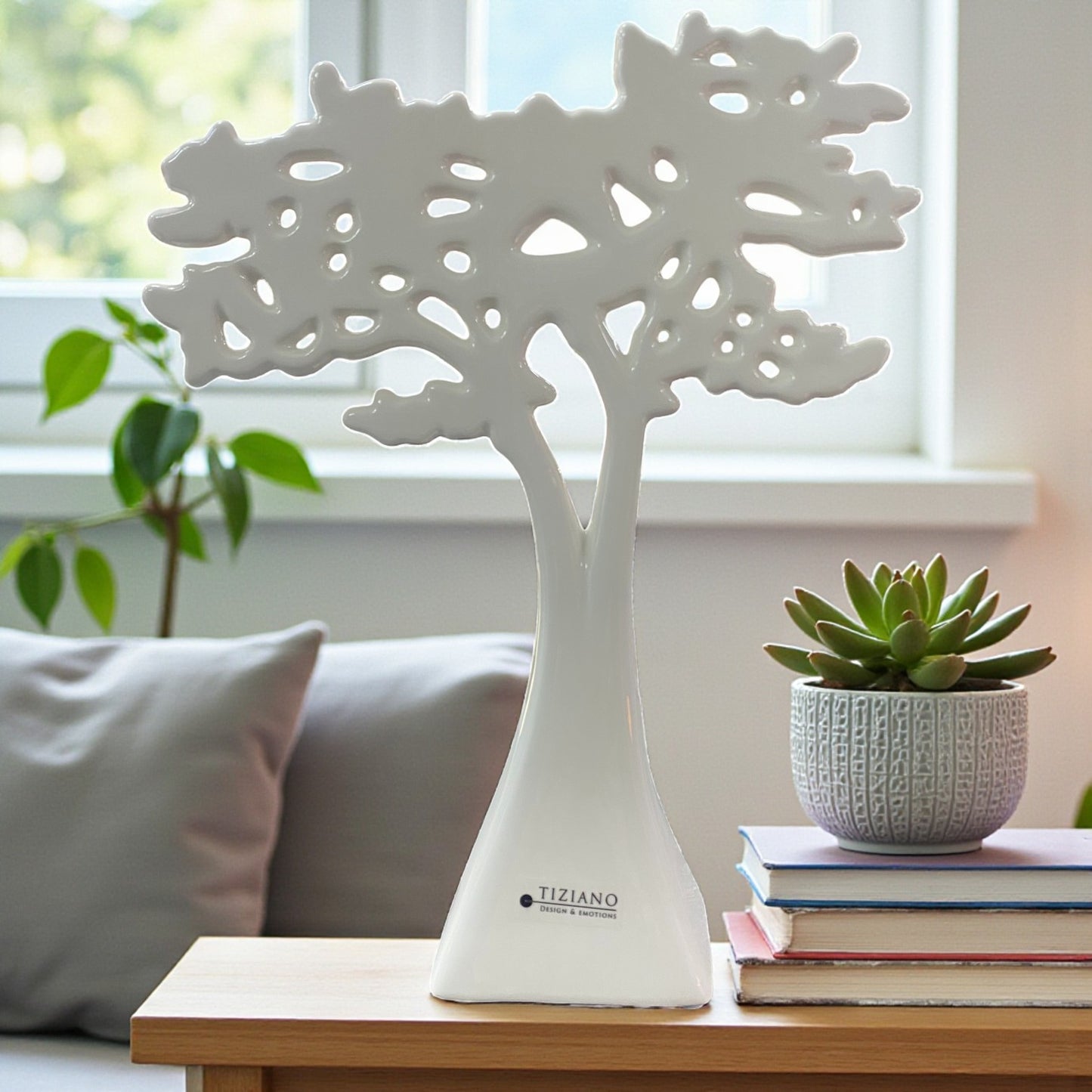Ein einzelner dekorativer Keramikbaum in Weiß steht auf einem Tisch vor einem Fenster; das filigrane, durchbrochene Kronendesign wirkt modern und leicht.