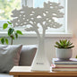Ein einzelner dekorativer Keramikbaum in Weiß steht auf einem Tisch vor einem Fenster; das filigrane, durchbrochene Kronendesign wirkt modern und leicht.