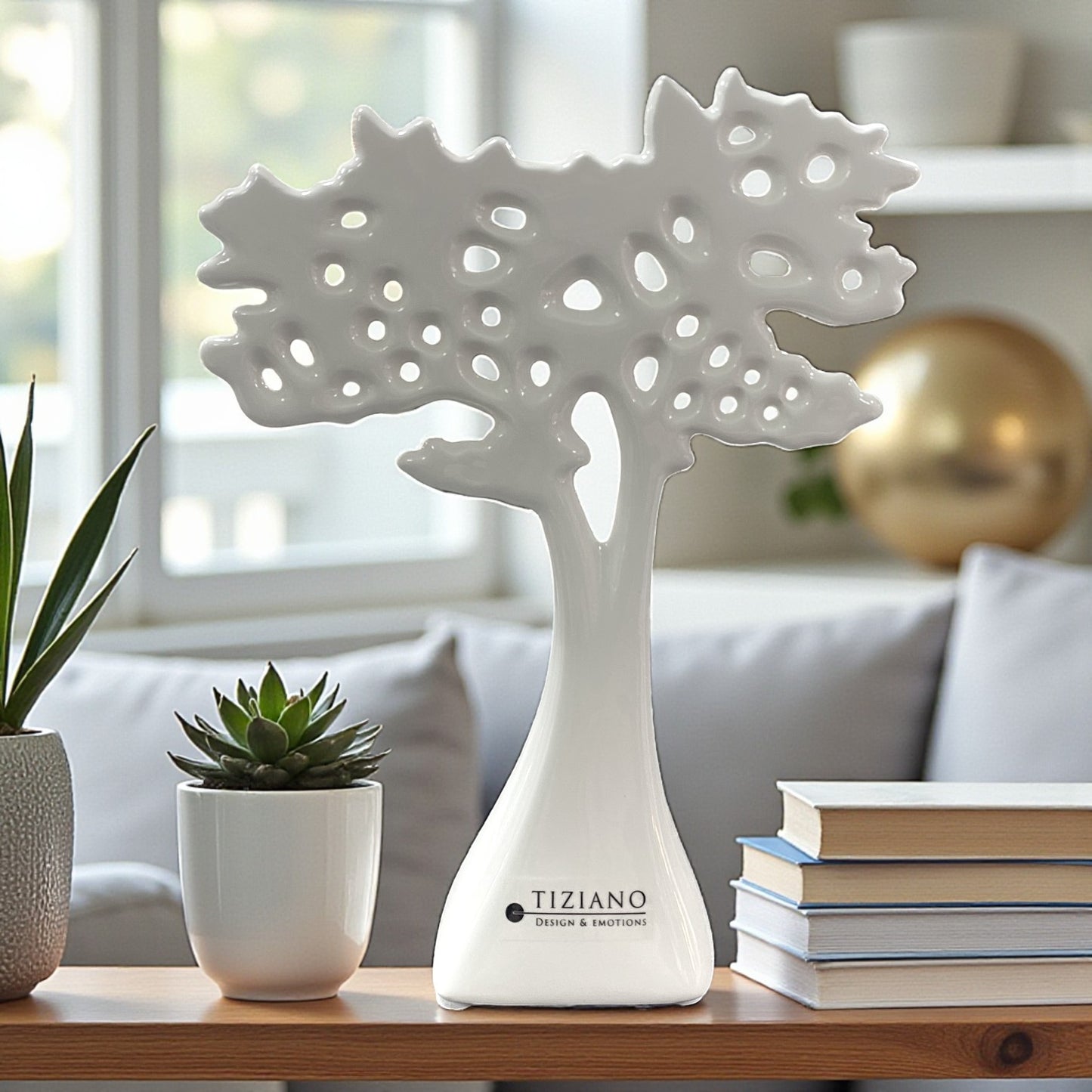 Ein weißer Keramikbaum mit durchbrochener, strukturierter Baumkrone steht als Dekoelement auf einem Tisch neben einem Sukkulententopf und Büchern.